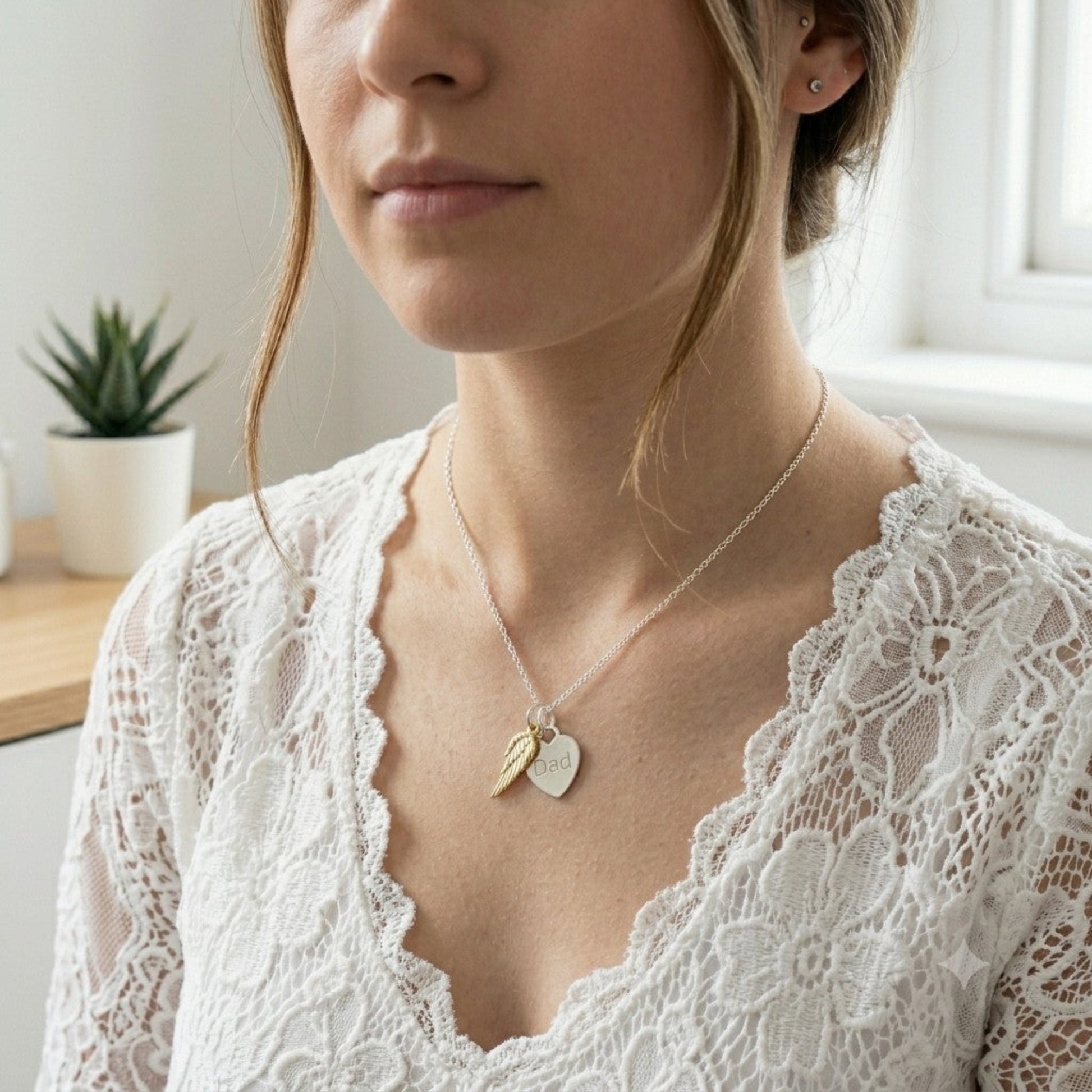A sterling silver heart engraved with the word "Dad" sits next to a gold vermeil angel wing.