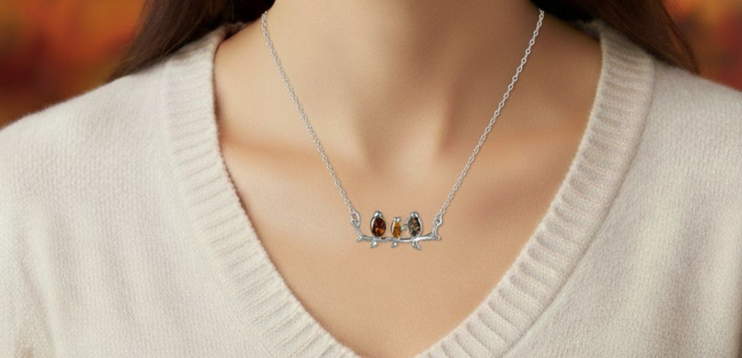 Sterling silver connector necklace showing three birds on a branch. The birds are inlaid with three types of amber - honey, cognac and olive. Shown worn.
