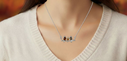 Sterling silver connector necklace showing three birds on a branch. The birds are inlaid with three types of amber - honey, cognac and olive. Shown worn.