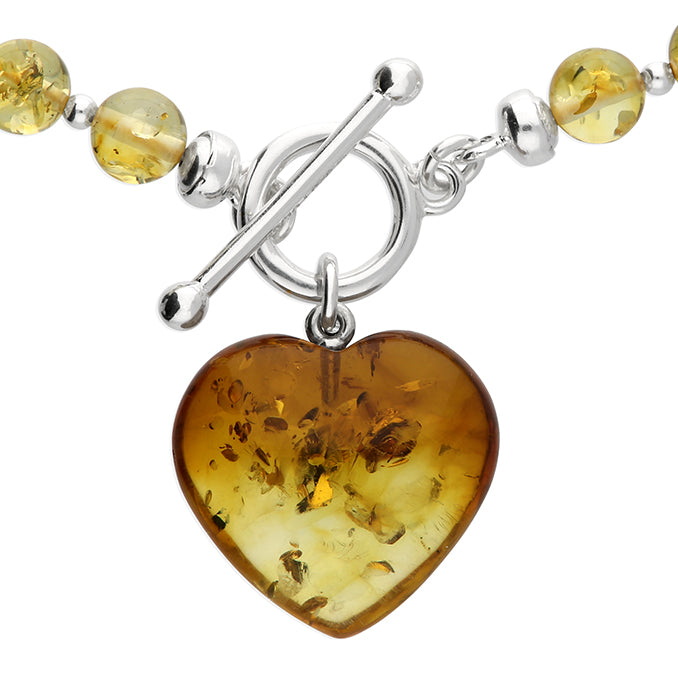 Cognac amber necklace fastened with sterling silver TBar clasp showing close up of dangling heart charm. 