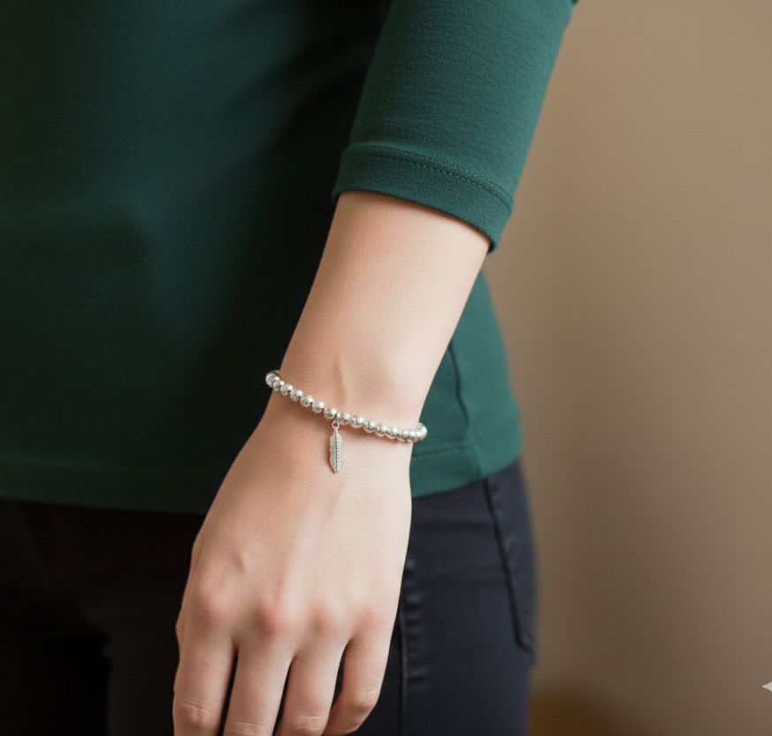 Sterling silver beaded bracelet with a feather charm shown worn