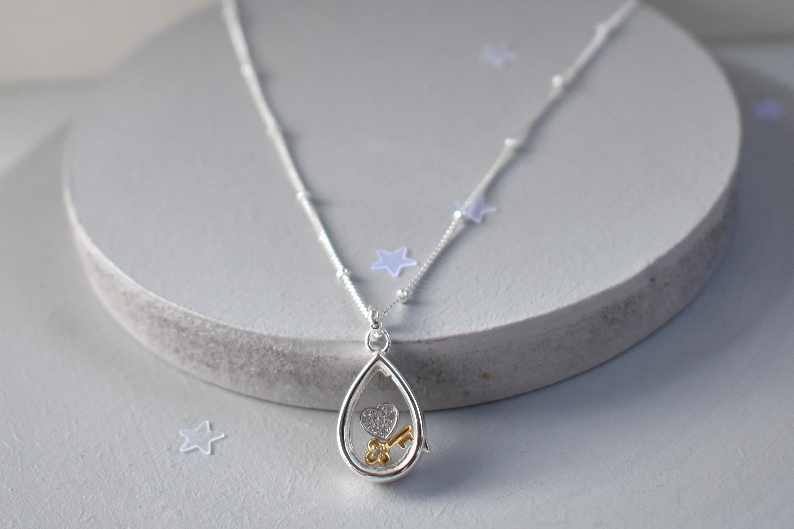 Sterling silver pear-shaped glass locket with tiny heart and key charms on a beaded chain