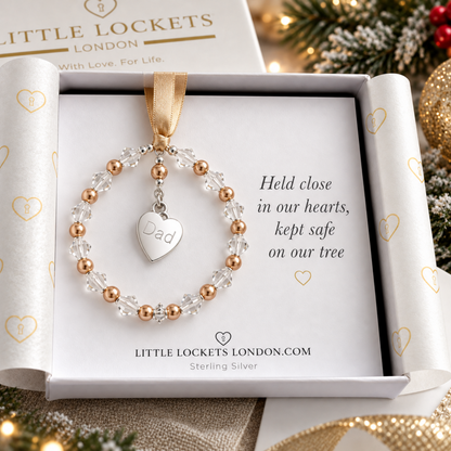 A personalized Christmas ornament shaped like a beaded ring with a dangling heart charm engraved with the word 'Dad'. The ornament features pearls interspersed with high quality Austrian crystals. Shown gift boxed and mounted on card with the words "Held close in our hearts, kep safe on our tree".