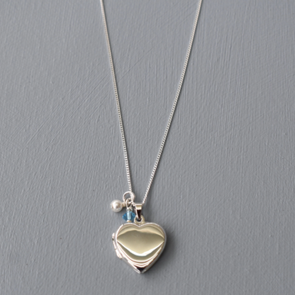 sterling silver heart locket, opens to allow for two photos to be fitted. Finished with a white glass pearl and tiny blue crystal.