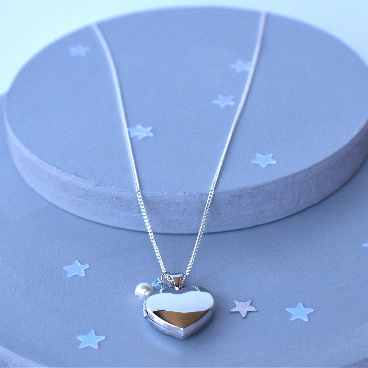 sterling silver heart locket, opens to allow for two photos to be fitted. Finished with a white glass pearl and tiny blue crystal.