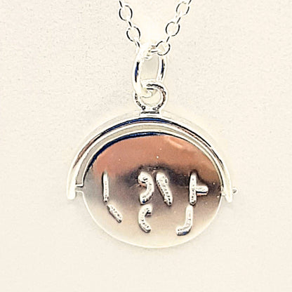 Sterling silver pendant with markings on both sides. When the disc is spun, it forms the words "I  LOVE YOU"