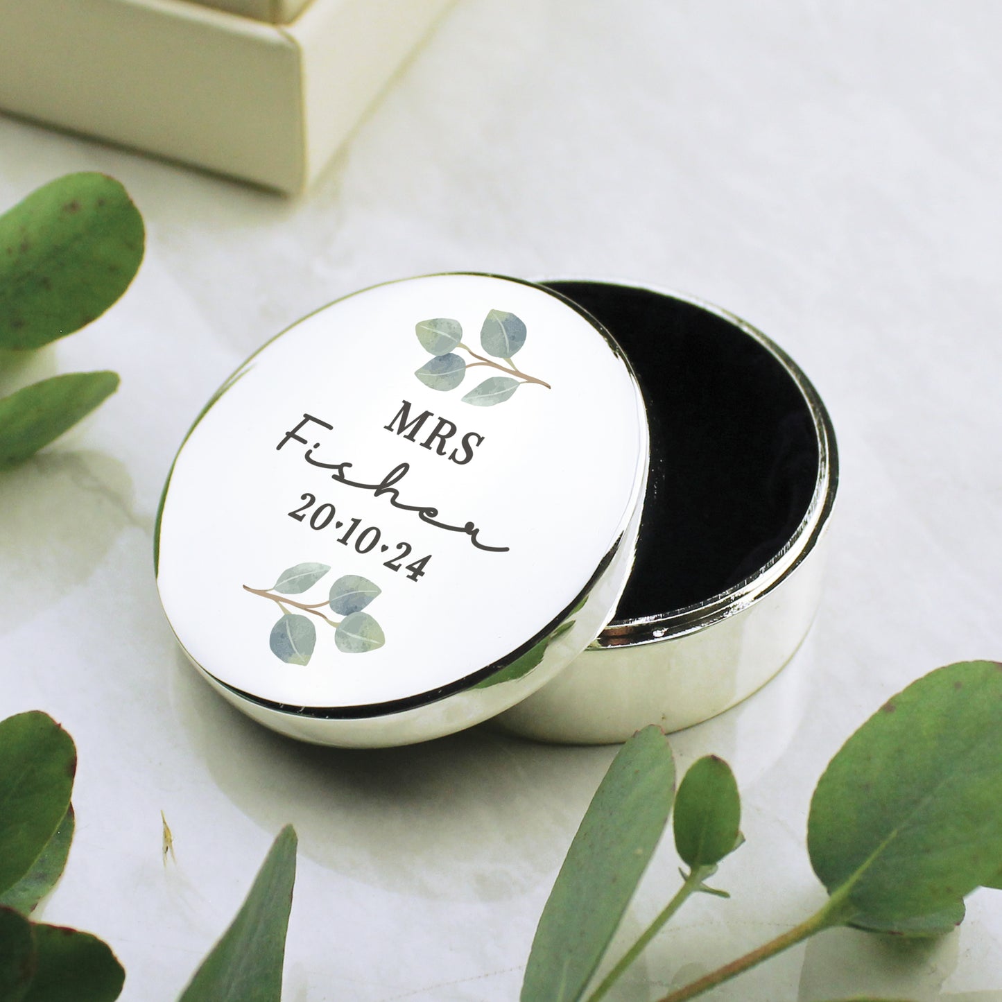 A round silver colour ring box with tiny leaves and an inscript of Mr & Mrs, surname and the wedding date