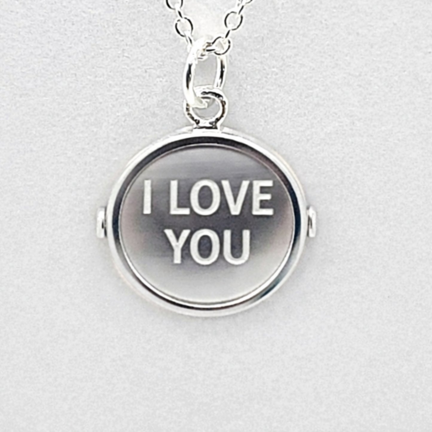 Simulated view of sterlnng silver pendant with markings on both sides that, when spun, form the words "I LOVE YOU"