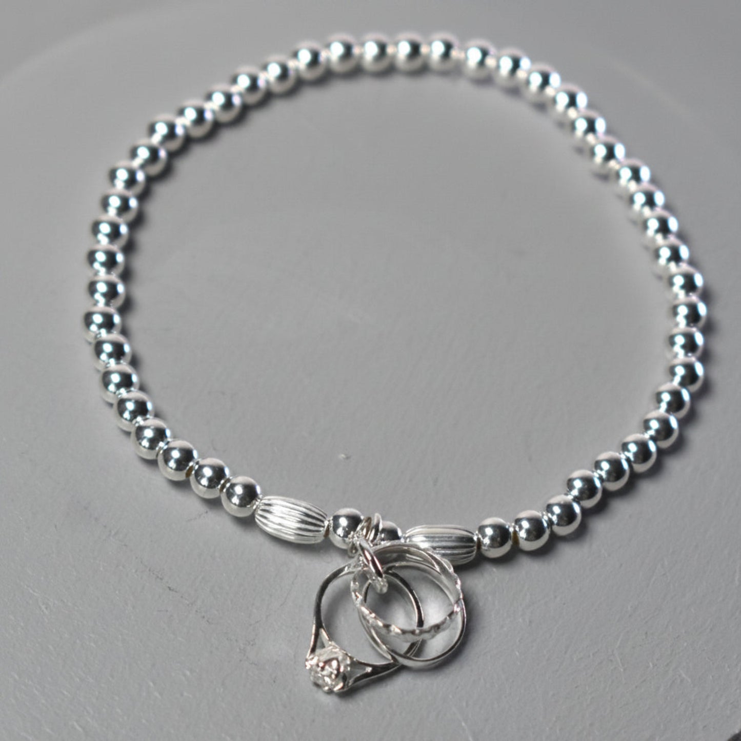 4mm sterling silver beads make this elasticated bracelet finished with three rings symbolising engagement, wedding and eternity rings