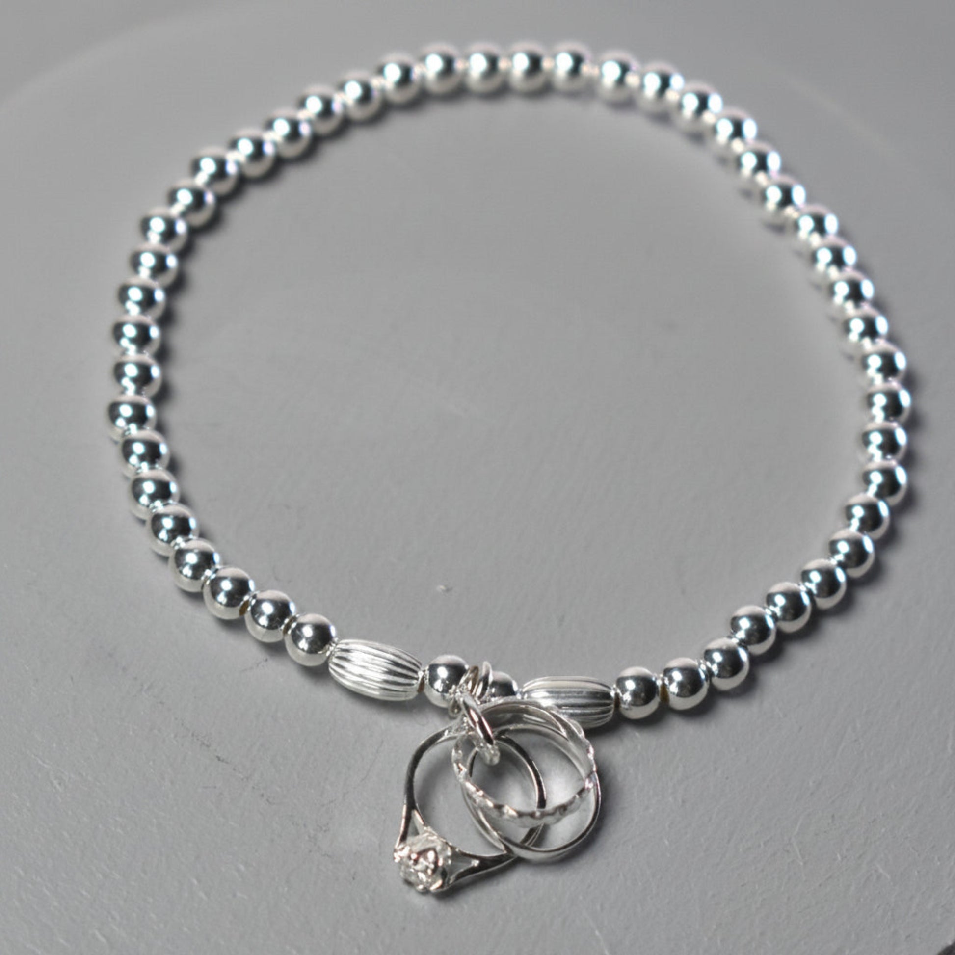 4mm sterling silver beads make this elasticated bracelet finished with three rings symbolising engagement, wedding and eternity rings