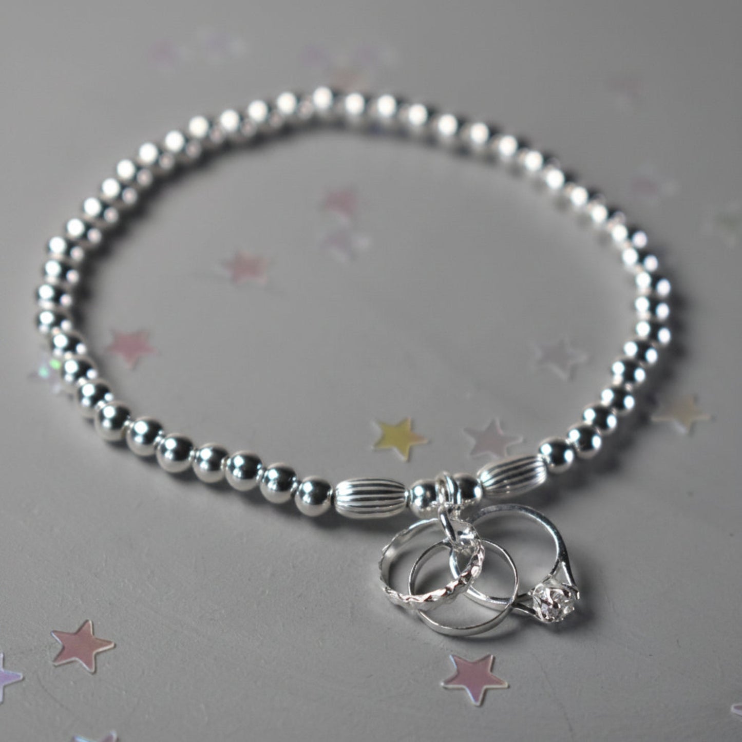 An elasticated sterling silver beaded bracelet with 4mm beads finished with a sterling silver charm of three rings symbolising engagement , wedding and eternity rings. 