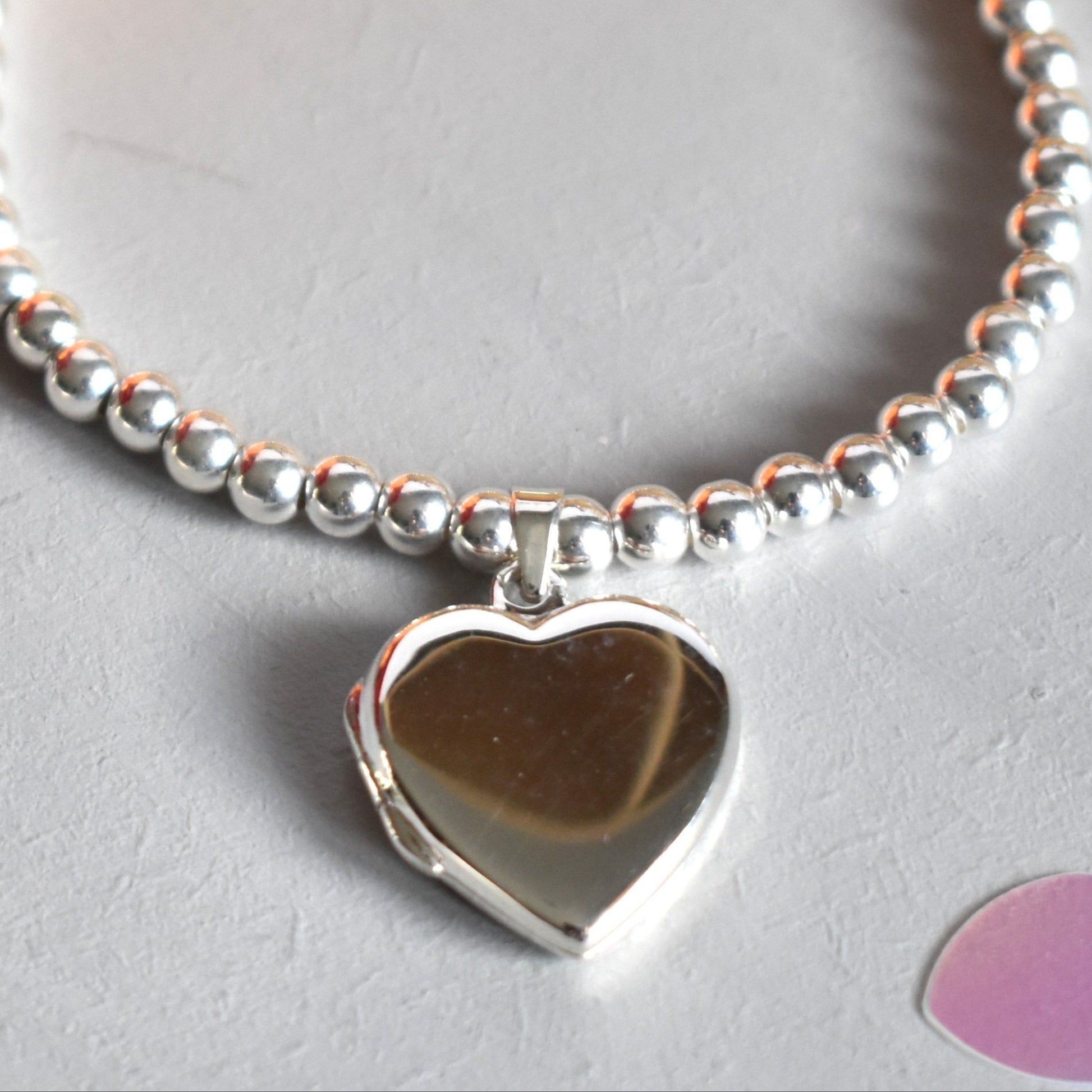sterling silver beads are threaded onto strong elastic and finished with a sterling silver heart shaped locket which opens for you to add up to two photos.