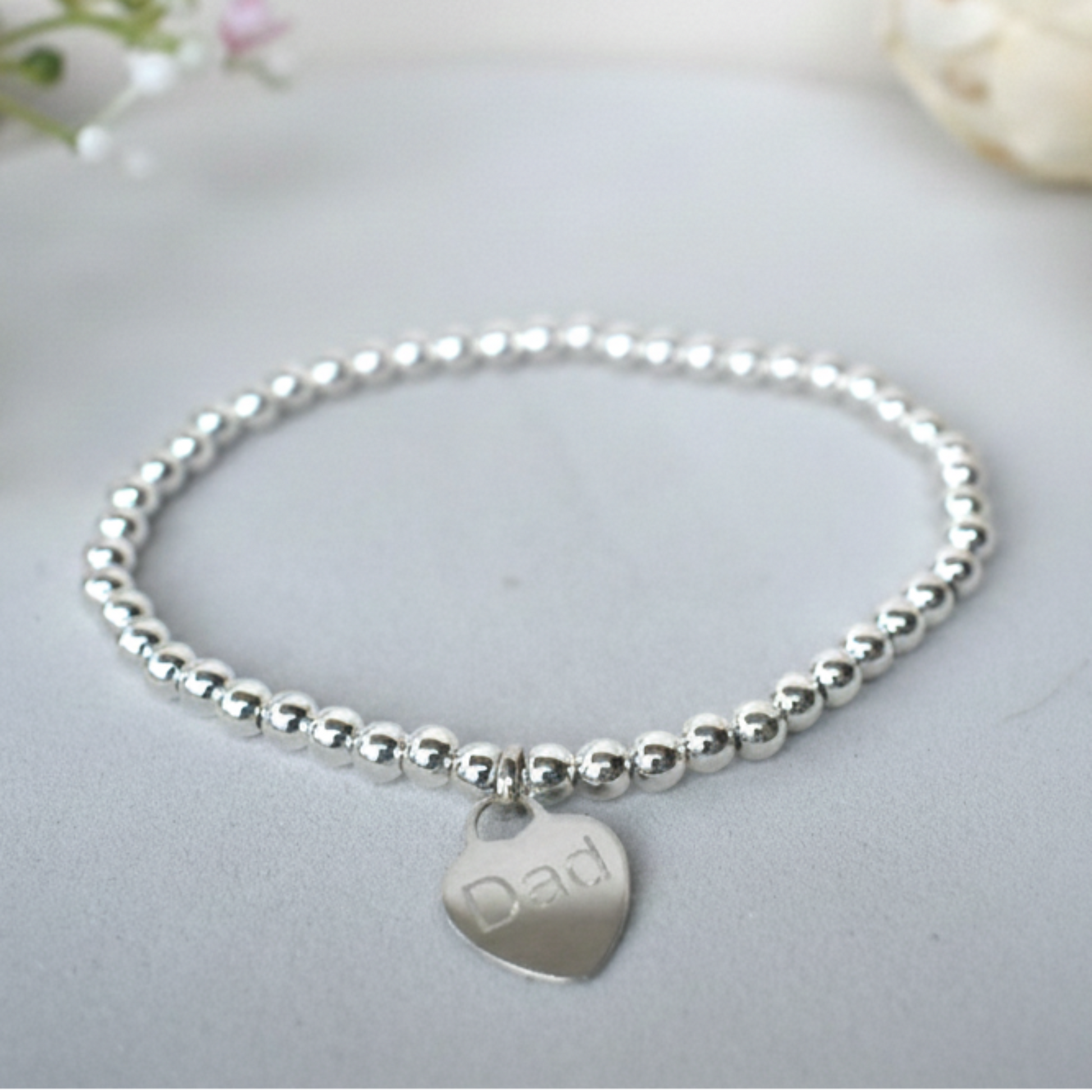 Silver beaded bracelet  of 4mm sterling silver beads threaded on strong elastic with a suspended sterling silver heart that can be engraved with wording of your choice. 