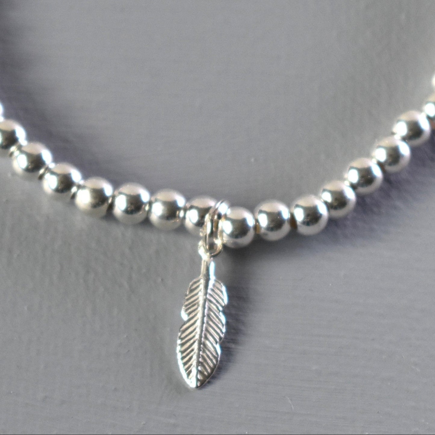 Close up of sterling silver bracelet showing 4mm sterling silver beads threaded on to strong elastic and with a sterling silver feather charm. 