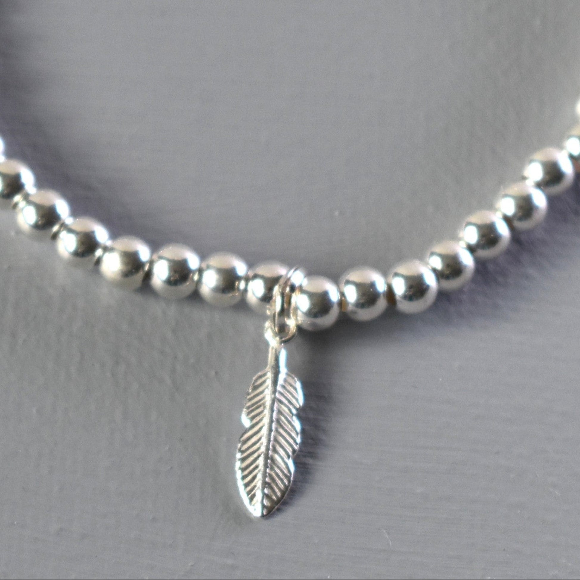 Close up of sterling silver bracelet showing 4mm sterling silver beads threaded on to strong elastic and with a sterling silver feather charm. 