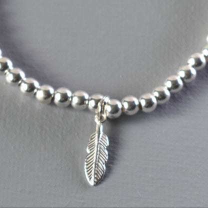 Close up of sterling silver bracelet showing 4mm sterling silver beads threaded on to strong elastic and with a sterling silver feather charm. 