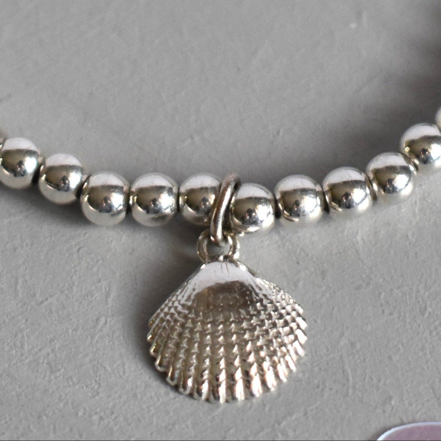 Close up of Sterling silver beaded bracelets with 4mm beads. Suspended from the bracelet  is a sterling silver clamshell. 