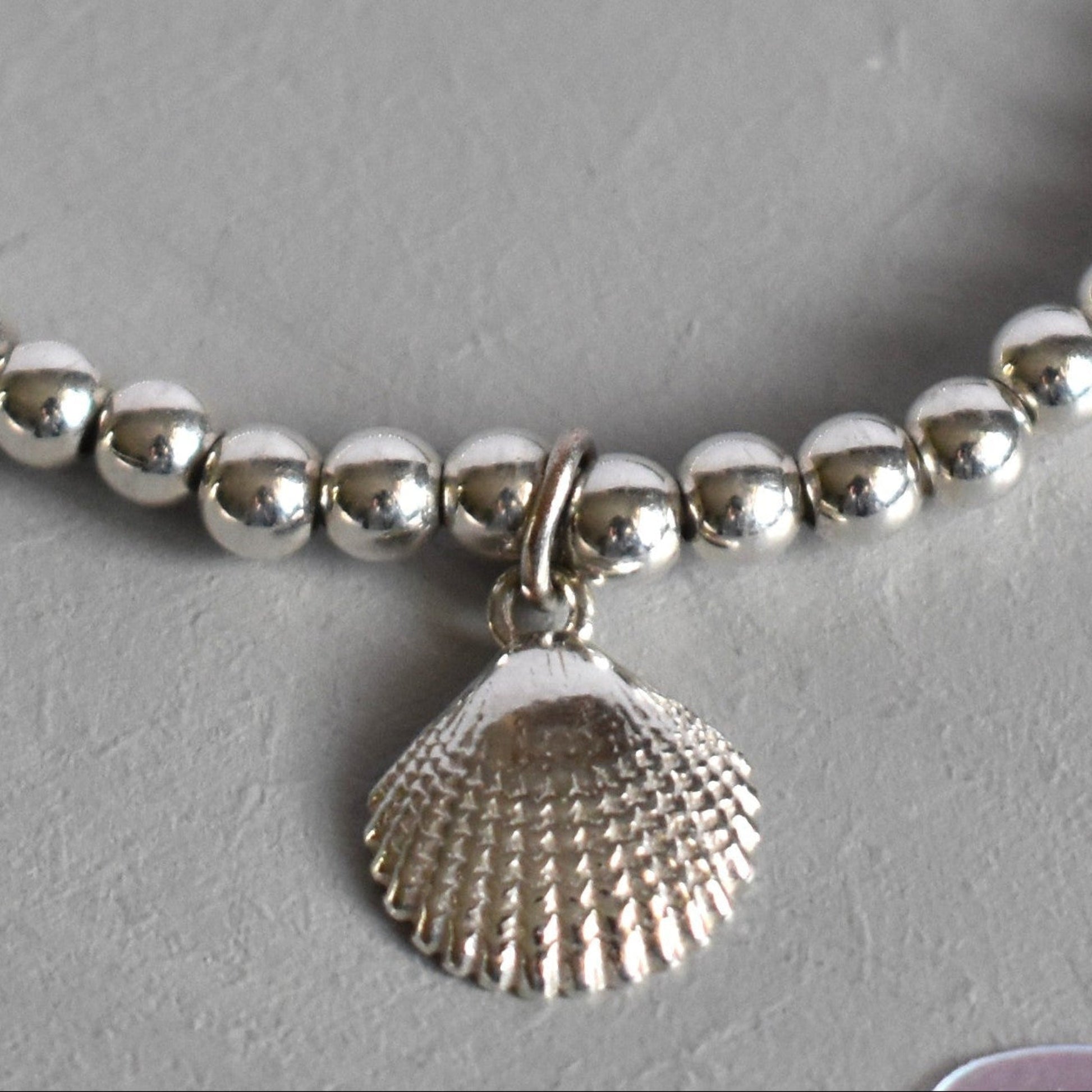 Close up of Sterling silver beaded bracelets with 4mm beads. Suspended from the bracelet  is a sterling silver clamshell. 