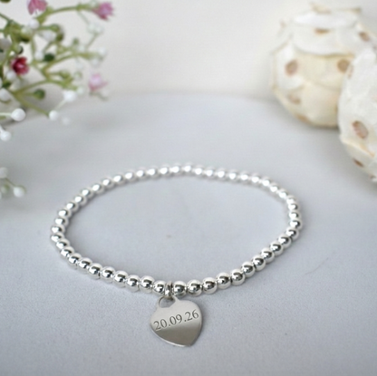 A sterling silver elasticated beaded bracelet carrying sterling silver  heart  engraved with a special date