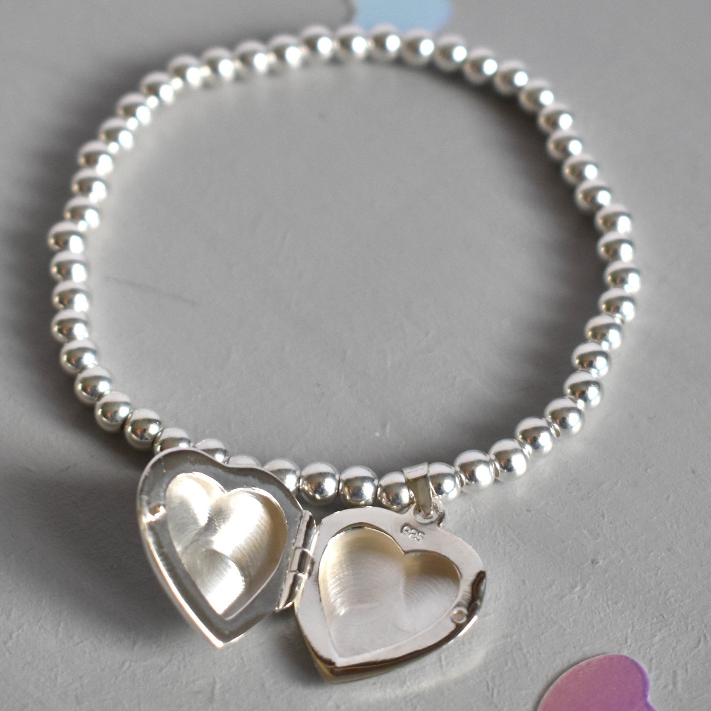 16mm heart shaped sterling silver locket suspended from 4mm sterling silver beads threaded onto strong elastic. The locket opens for you to add two photos of your choice. Shown open