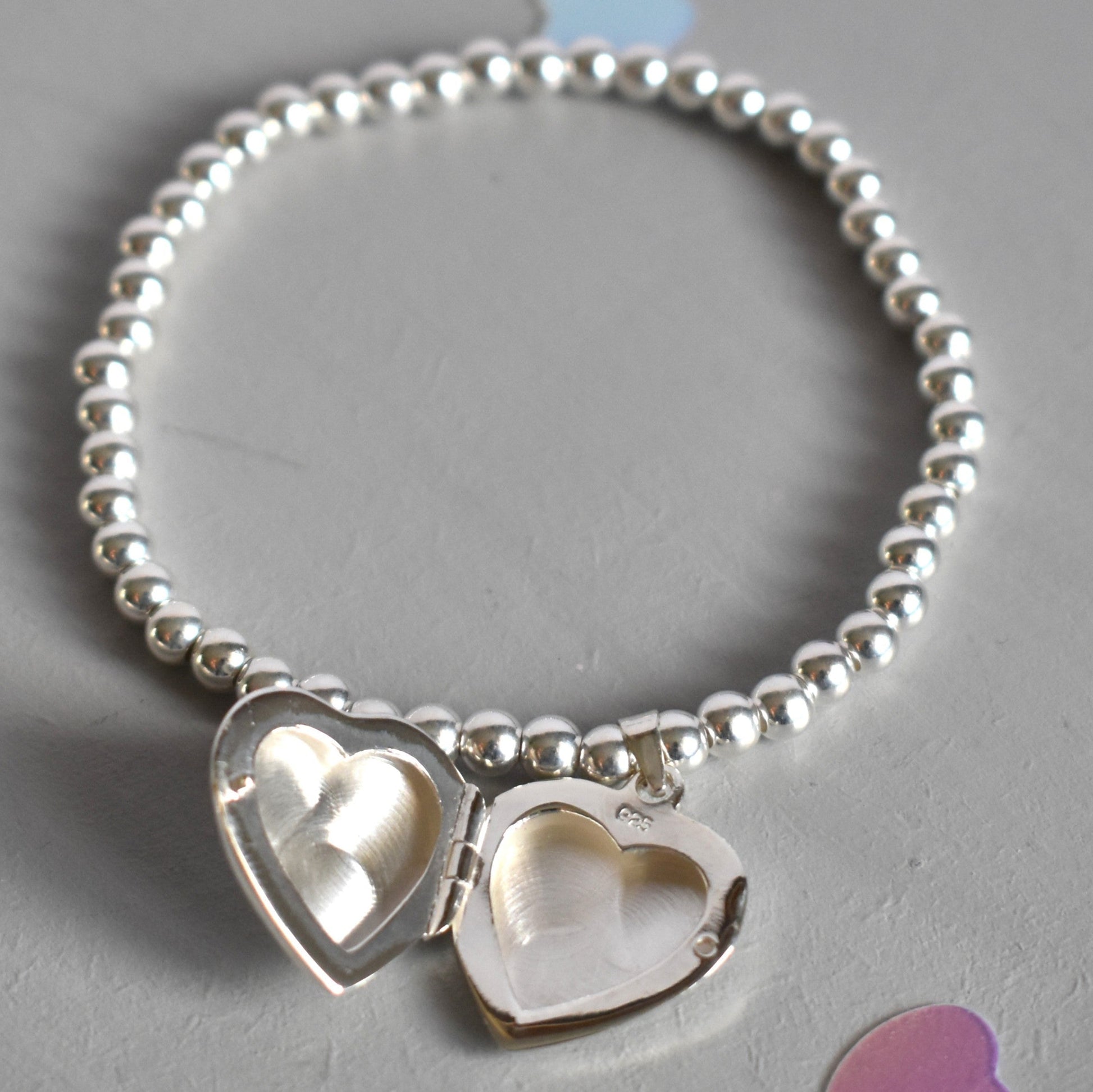 16mm heart shaped sterling silver locket suspended from 4mm sterling silver beads threaded onto strong elastic. The locket opens for you to add two photos of your choice. Shown open