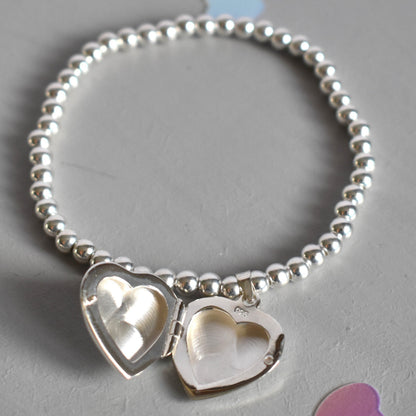 16mm heart shaped sterling silver locket suspended from 4mm sterling silver beads threaded onto strong elastic. The locket opens for you to add two photos of your choice. Shown open