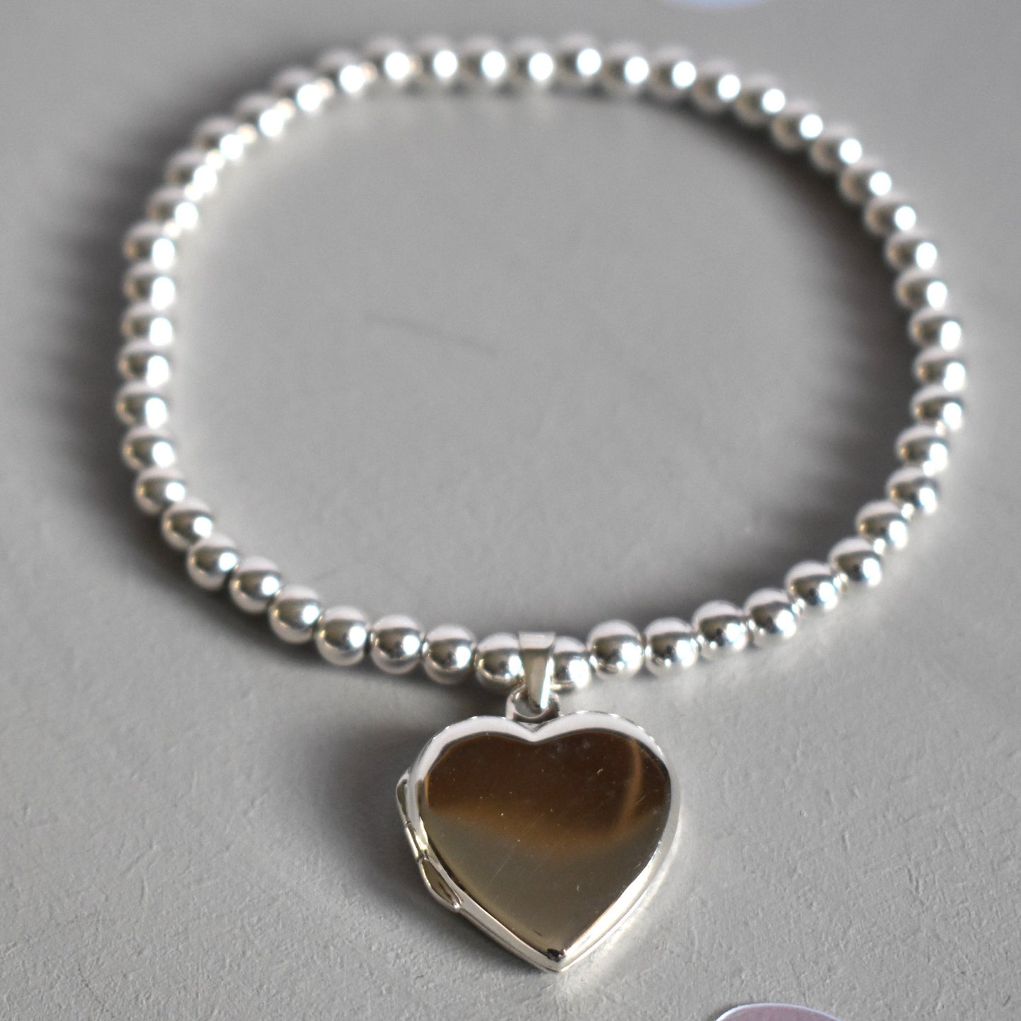 16mm heart shaped sterling silver locket suspended from 4mm sterling silver beads threaded onto strong elastic. The locket opens for you to add two photos of your choice.
