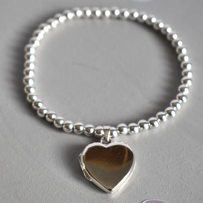 16mm heart shaped sterling silver locket suspended from 4mm sterling silver beads threaded onto strong elastic. The locket opens for you to add two photos of your choice.