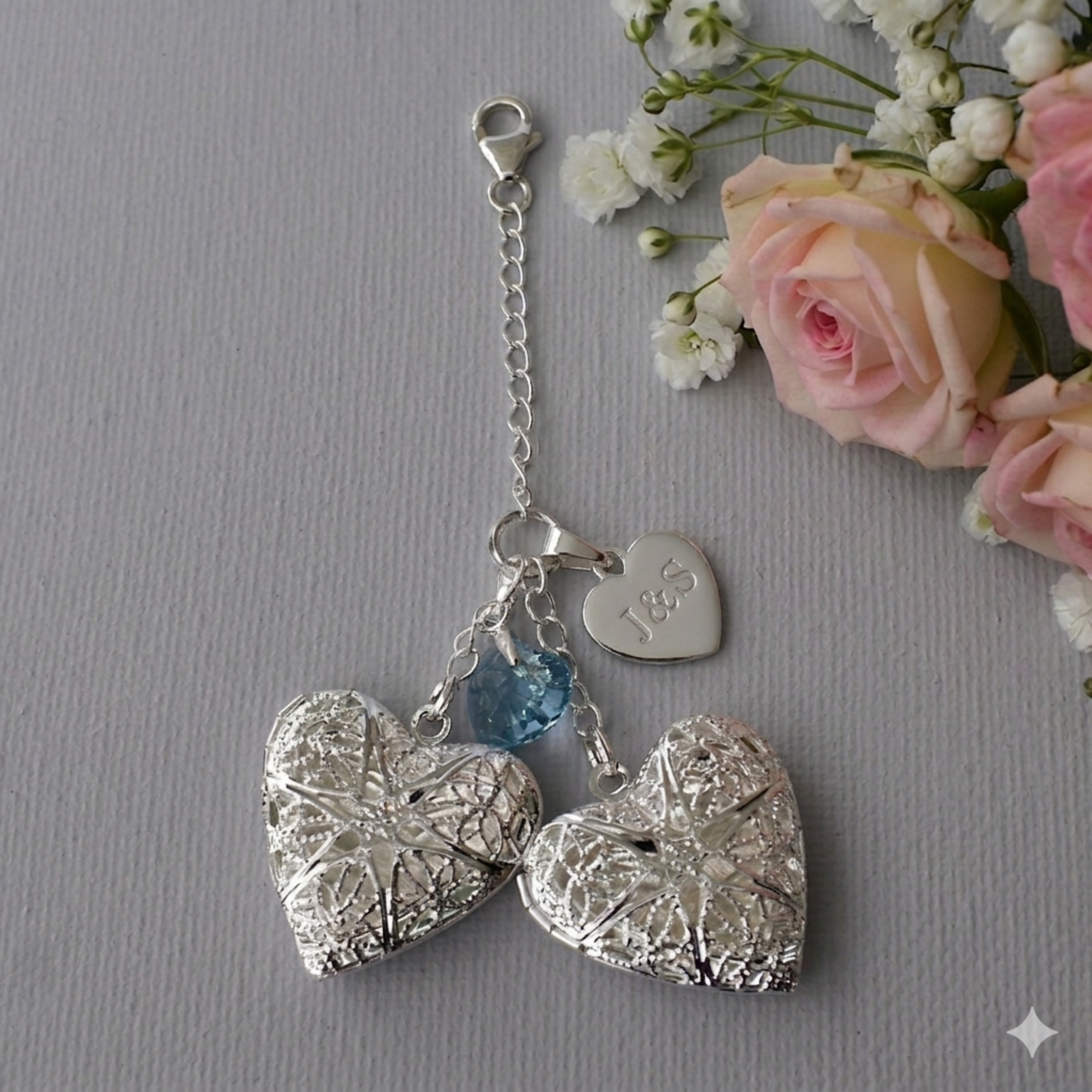 Two filigree lockets and a crystal blue heart are suspended from sterling silver chain for a wedding bouquet charm. An optional engraved sterling silver heart can be added to the charm