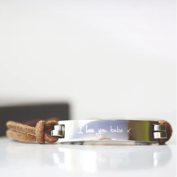 A brown leather bracelet with a central metal plate engraved with your own words and a silver lobster clasp