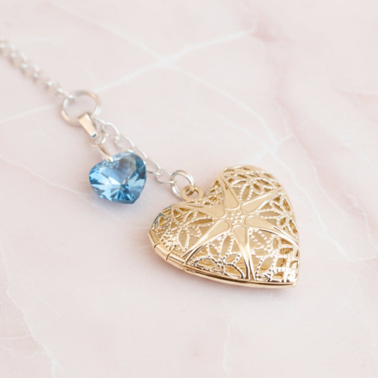 Wedding bouquet locket. A filigree locket that opens to take one photo is suspended from a sterling silver chain and next to a high quality pale blue crystal heart. The chain ends in a lobster clasp so that the charm can be fastened securely to th Bride's bouquet