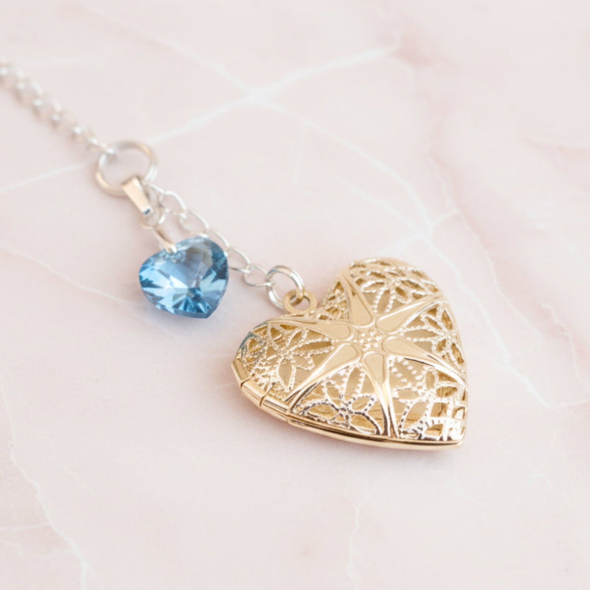 Wedding bouquet locket. A filigree locket that opens to take one photo is suspended from a sterling silver chain and next to a high quality pale blue crystal heart. The chain ends in a lobster clasp so that the charm can be fastened securely to th Bride's bouquet