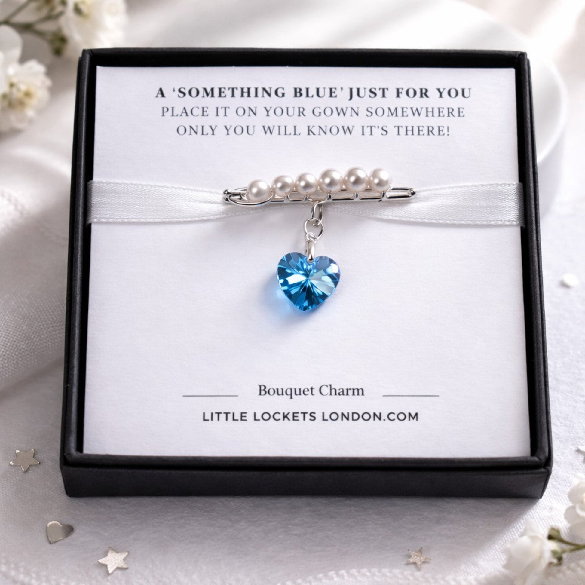 A sterling silver safety pin is finished with 4mm white glass pearls The loop on the pin hold a sterling silver bail with the highest quality blue crystal heart. Shown in gift box.