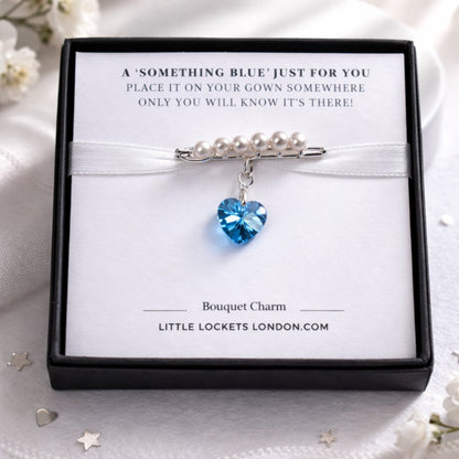 A sterling silver safety pin is finished with 4mm white glass pearls The loop on the pin hold a sterling silver bail with the highest quality blue crystal heart. Shown in gift box.
