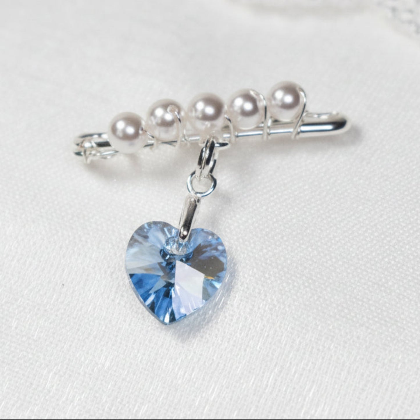 A sterling silver safety pin is finished with 4mm white glass pearls The loop on the pin hold a sterling silver bail with the highest quality blue crystal heart. The pin can be pinned to a wedding bouquet or worn inside the wedding gown as a secret something blue.
