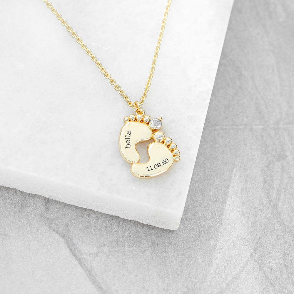 Personalised baby feet necklace. Engraved with baby’s name and date of birth on adjustable necklace. Shown in gold plate.