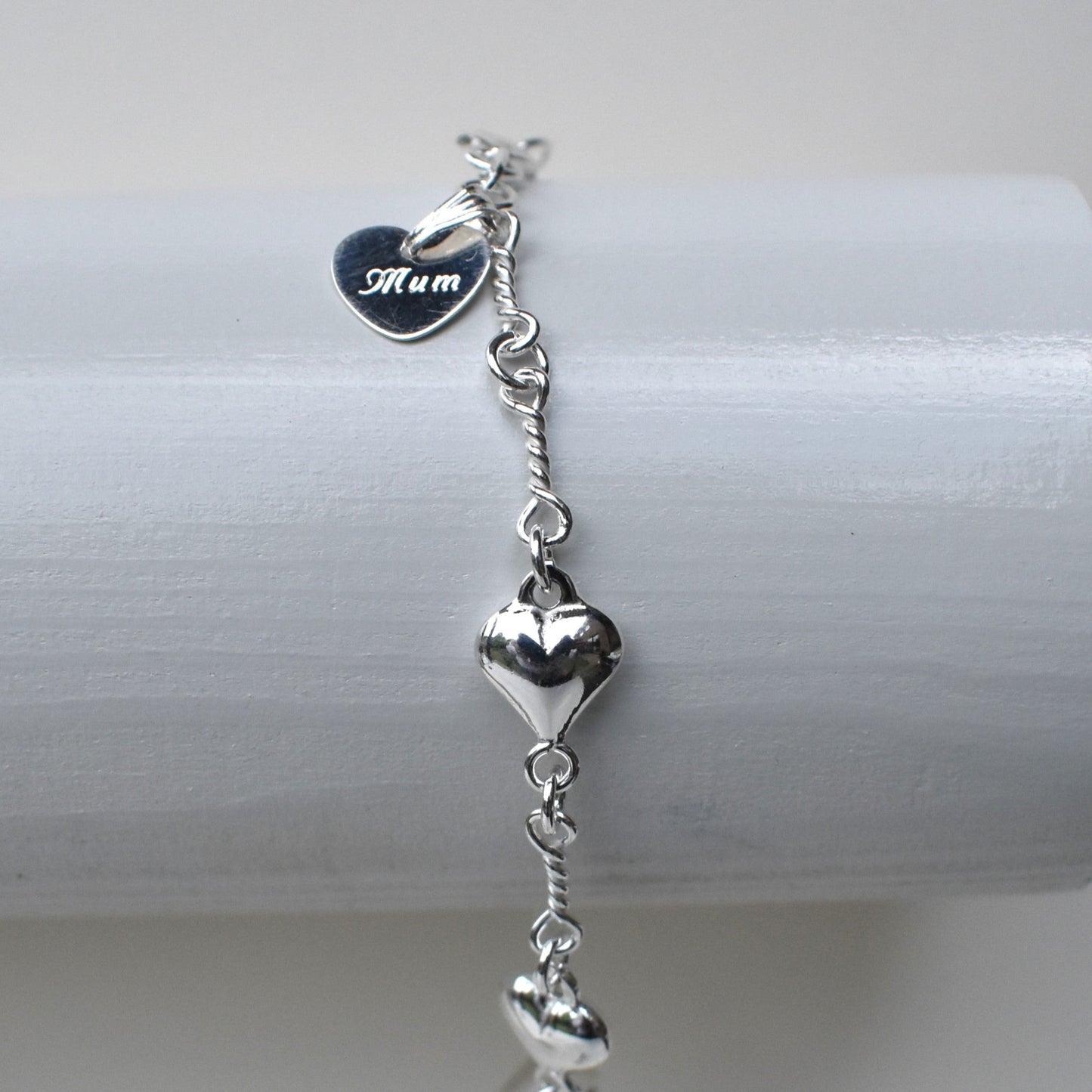 Sterling silver puffed hearts linked together by long twisted links. Next to the fastener is a small 10mm sterling silver heart engraved with a name of our choice.