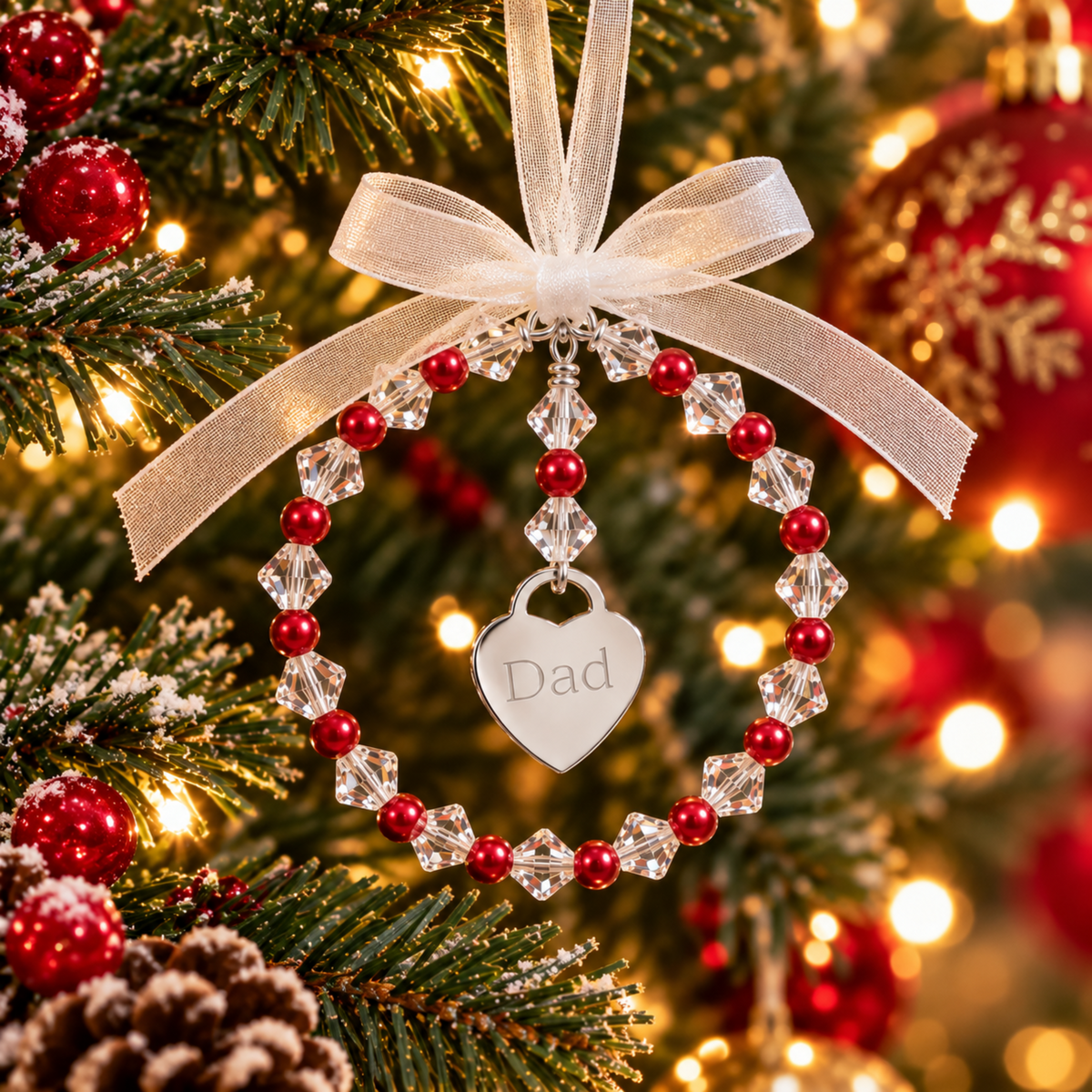 A personalized Christmas ornament shaped like a beaded ring with a dangling heart charm engraved with the word 'Dad'. The ornament features red pearls interspersed with high quality Austrian crystals. Complete with ribbon, ready for you to hang on the christmas tree.