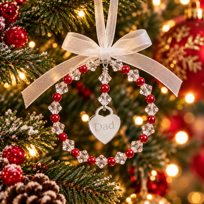 A personalized Christmas ornament shaped like a beaded ring with a dangling heart charm engraved with the word 'Dad'. The ornament features red pearls interspersed with high quality Austrian crystals. Complete with ribbon, ready for you to hang on the christmas tree.