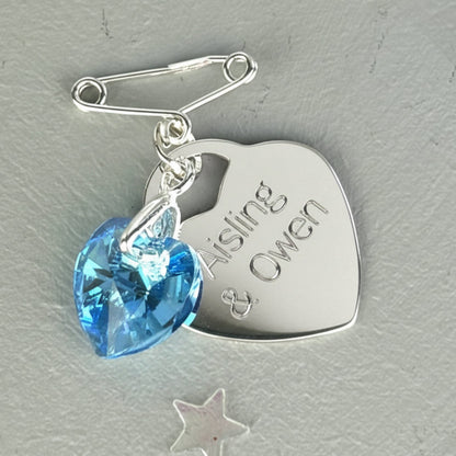 Blue crystal heart suspended from a sterling silver bail and a tiny sterling silver pin. Shown with a sterling silver heart engraved with the names of the couple.
