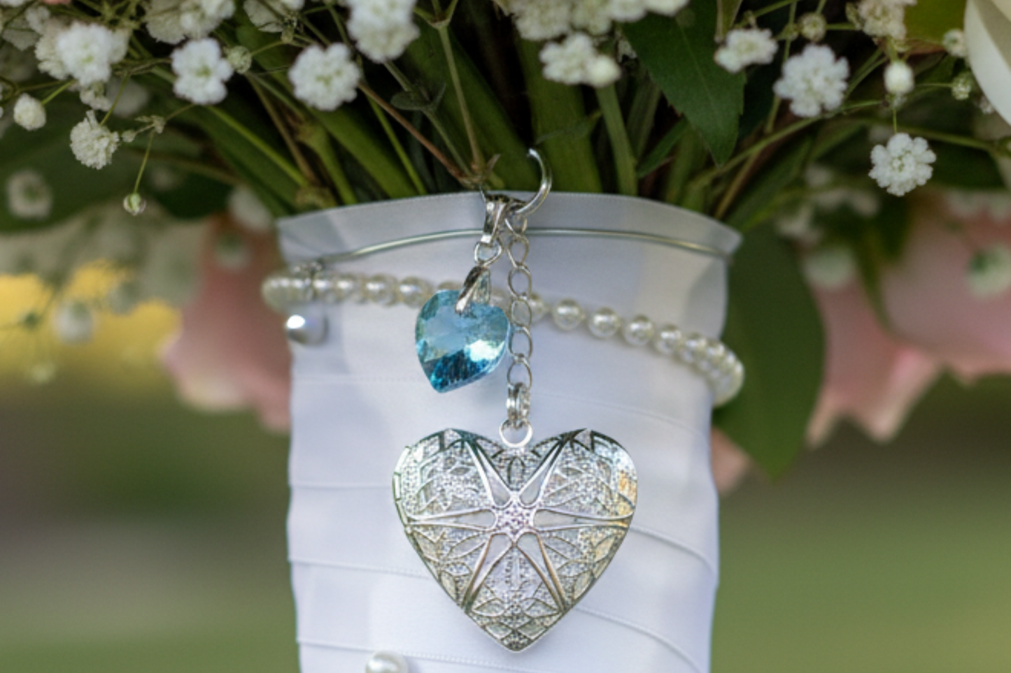 Wedding bouquet locket. A filigree locket that opens to take one photo is suspended from a sterling silver chain and next to a high quality pale blue crystal heart. The chain ends in a lobster clasp so that the charm can be fastened securely to th Bride's bouquet