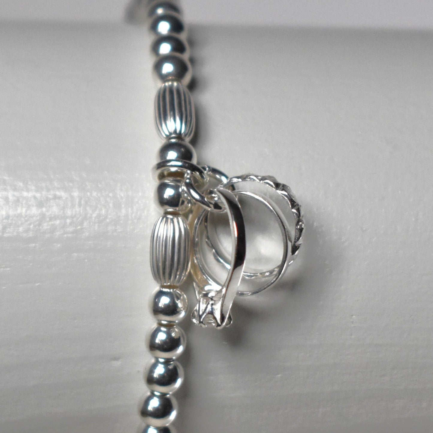 Sterling silver beads are threaded onto strong elastic and finished with a sterling silver charm symbolising engagement, wedding and eternity rings. 