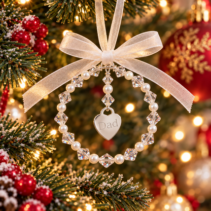 A personalized Christmas ornament shaped like a beaded ring with a dangling heart charm engraved with the word 'Dad'. The ornament features white pearls interspersed with high quality Austrian crystals. Complete with ribbon, ready for you to hang on the christmas tree.