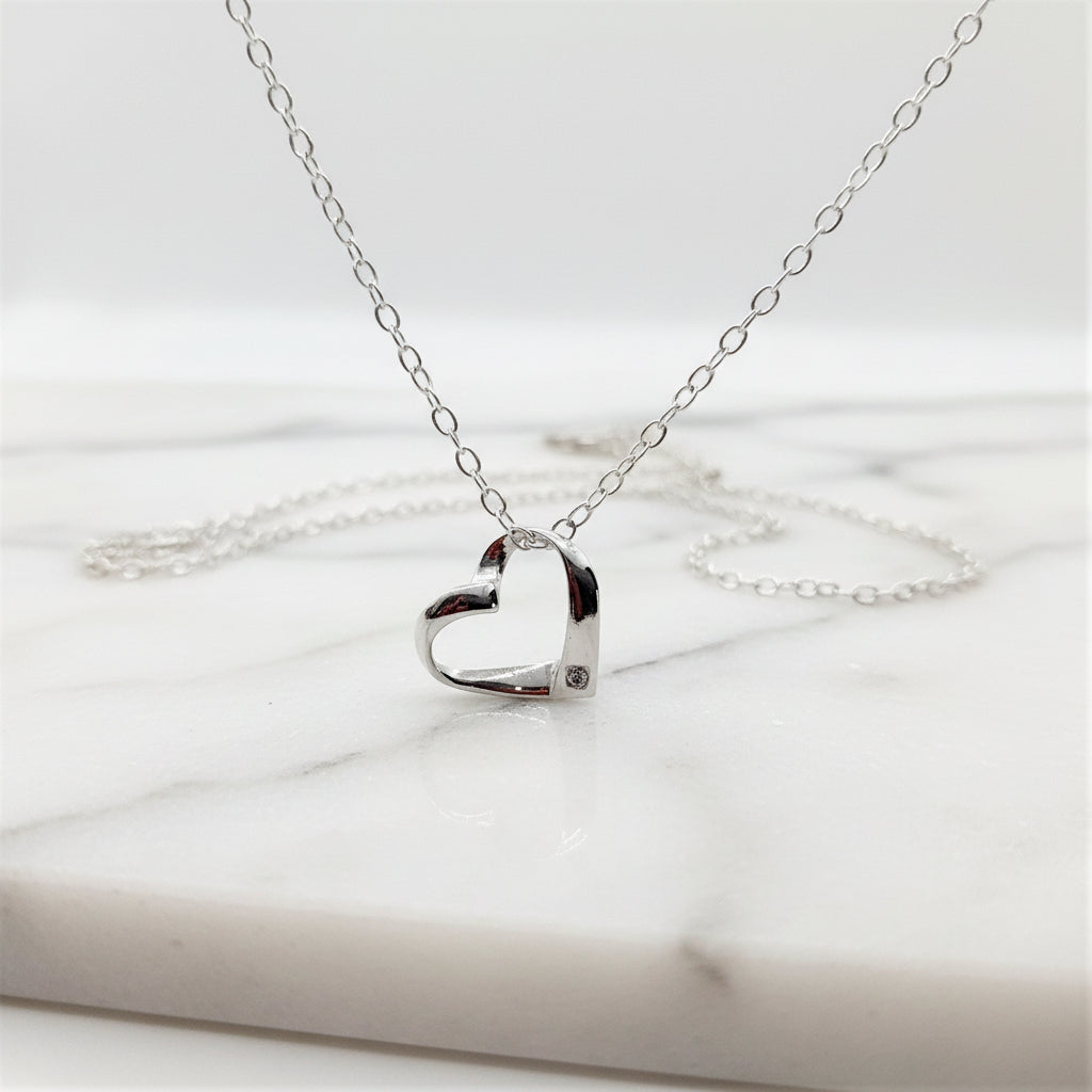 Sterling silver ribbon style heart with a tiny zircona at the base is suspended from a sterling silver chain a