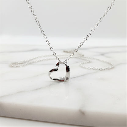 Sterling silver ribbon style heart with a tiny zircona at the base is suspended from a sterling silver chain a